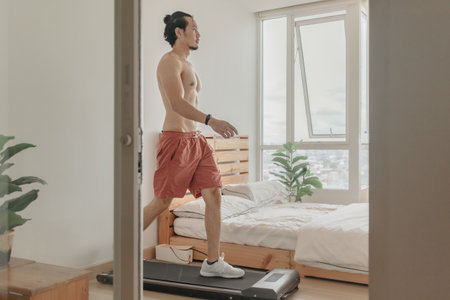 Asian man exercise by walking on the treadmill in his apartment.の写真素材