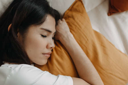 Asian woman is taking a nap or sleep on the sofa with yellow pillow.の写真素材
