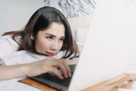 Asian woman works with laptop on the bed in concept of workation.