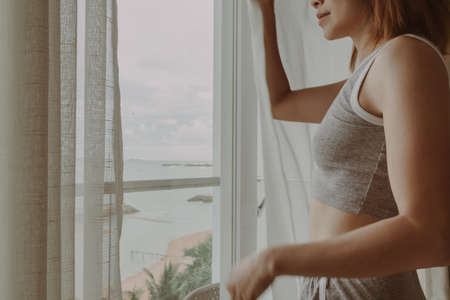 Attractive Asian woman look at the view behind the curtain in the hotel.の写真素材