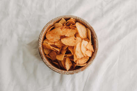 Bowl of potato chips on white sheet bed with hand picking up.の写真素材