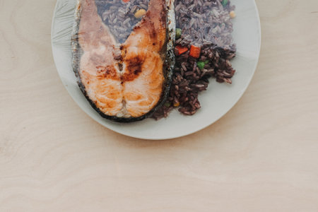 Cooked salmon steak with fried rice on the dish and sealed with plastic.の写真素材