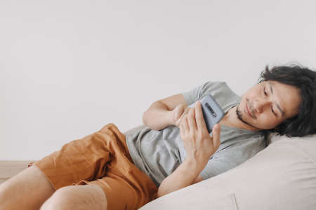 Asian man use smartphone while sit and relax on bean bag sofa.の写真素材