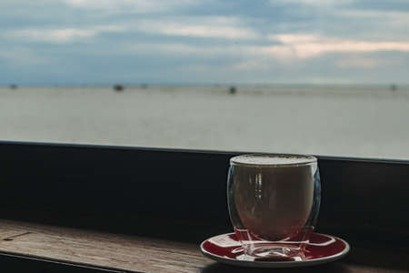 Cup of coffee on the wooden bar with evening sea view.の写真素材