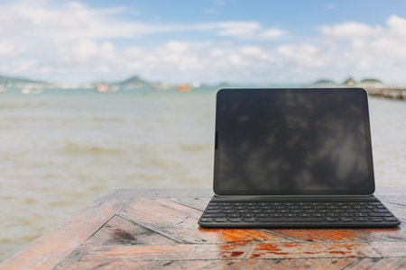 Black tablet with keyboard on wooden table and sea view in concept of workation.の写真素材