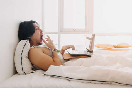 Asian man wake up and work with laptop on the bed first thing in the morning.の写真素材