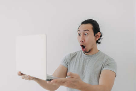 Shocked and surprised face of Asian man looking at the laptop in his hand.の写真素材