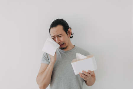 Crying face of Asian man with hand holding tissue isolated on white background.の写真素材