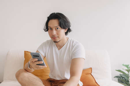 Freelance long hair Asian man sit on the sofa and use application smartphone.