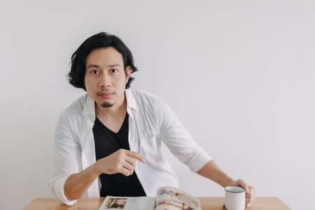 Asian man in white shirt reading magazine and drink coffee on wooden table.の写真素材