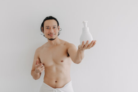 Happy Asian man wear towel and holding a big bottle of skincare product.の写真素材