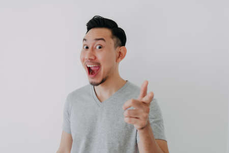 Wow face of Asian man wear grey t-shirt advertising a product on white wall.