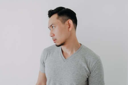 Straight face portrait of serious Asian man in grey t-shirt on white wall.の写真素材