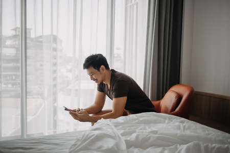 Asian man feels happy with his phone result while on vacation in the hotel.の写真素材