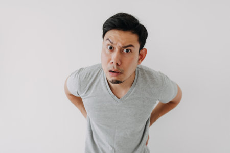Funny obvious peeking Asian man in grey t-shirt isolated on white background.の写真素材