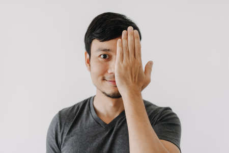 Smile face happy asian man with one eye close cover by hand isolated on white
