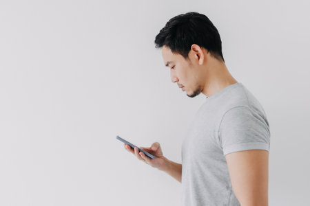 Asian man seriously concentrated on smartphone isolated on white background.の写真素材