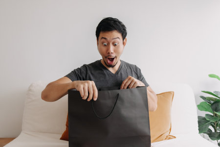 Funny surprised and shocked face of Asian man see product in the shopping bag.の写真素材