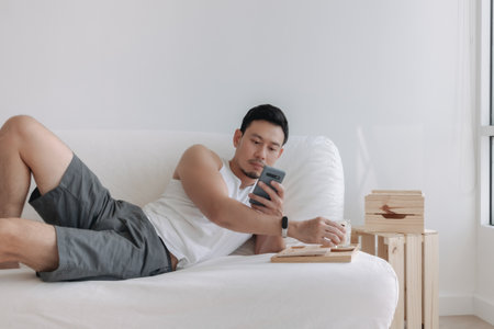 Asian man using mobile phone on his sofa in a relax day off at home. High quality photoの写真素材