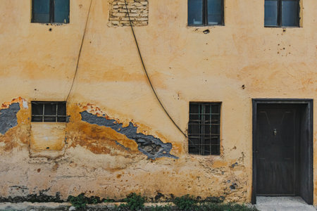Yellow old and damaged building with windows and door in old town.