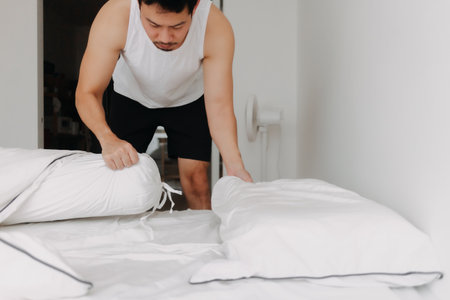 Asian man in white tank top is making bed folding into a sofa. High quality photoの写真素材