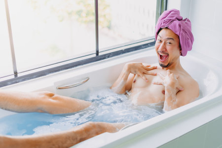 Funny asian man being childish and playful in the bathtub.