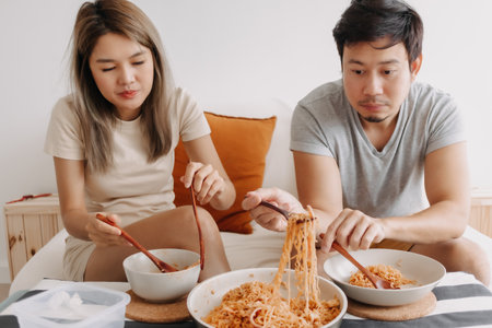 Funny asian couple lover eating quick noodle together.