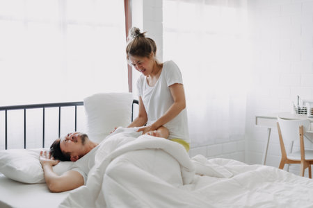 Funny lovely asian couple. Wife trying to wake husband up in the morning.の写真素材