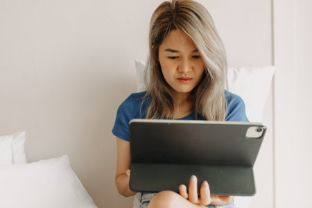 Serious asian woman working online with tablet on hotel bed in travel trip