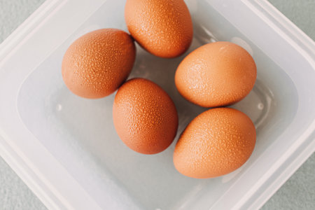 Pack of fresh eggs in white plastic box on grey table cover.