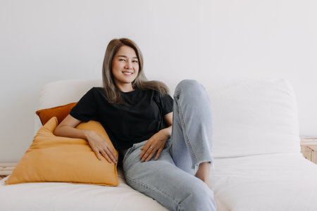 Happy asian woman sits and relax on sofa in one good fine day.の写真素材