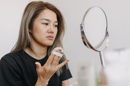 Asian woman wearing make up in front of the mirror in white bright room.の写真素材