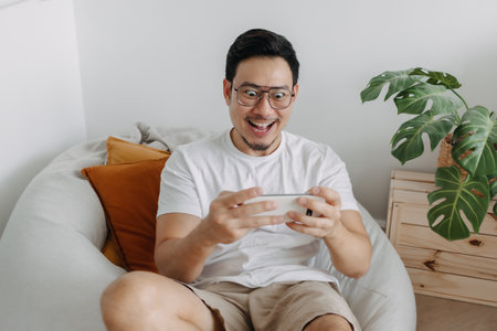 Happy face of asian man playing mobile game on a relax day in the living room.の写真素材