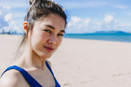 Asian woman walking on the sunny beach feeling the sun burn on her face skin.の写真素材