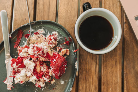 Messed up strawberry cake and cream on the dish with a cup of coffee.