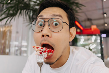 Funny happy face of asian man eating and putting cake into his mouth in the cafe