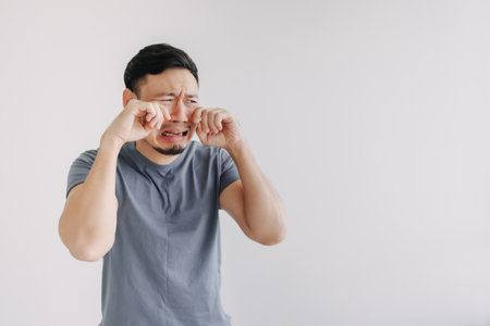 Sad funny face asian man in blue t-shirt crying stand isolated on white.の写真素材