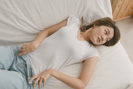 Cute asian woman zipping down her jean for her comfort lie on sofa in her home.の写真素材