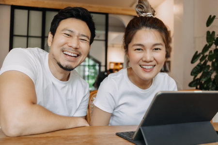 Happy laughing asian couple watching computer tablet together in the cafe.の写真素材