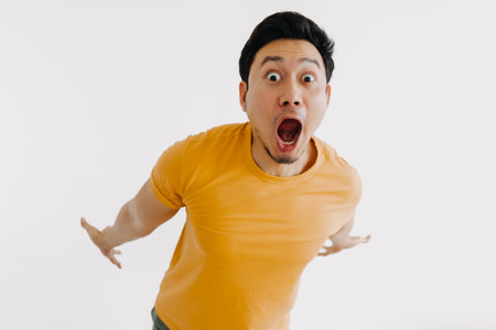 Shocked and surprised face of asian man jumping out isolated on white.