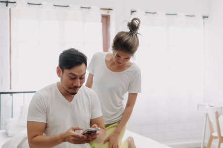 Funny asian couple. Wife peeking husband who chatting on the smartphone.の写真素材