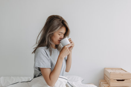 Asian woman drinking coffee right after wake up on the bed in the morning.の写真素材