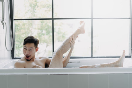 Funny asian man lying in the bathtub showing his leg pretend to be a sexy woman.の写真素材