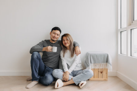 Happy romantic asian couple lover support with hug and coffee sit on the floor.の写真素材