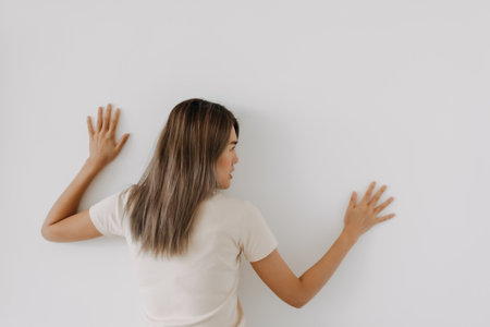 Funny asian woman lie on background try to spy and listen over the wall.の写真素材