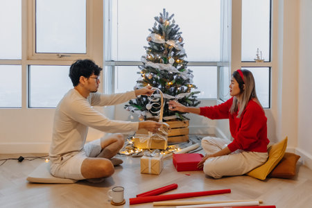 Asian husband and wife couple lover decorating Christmas tree together while the man helping woman packing decoration boxes.の写真素材