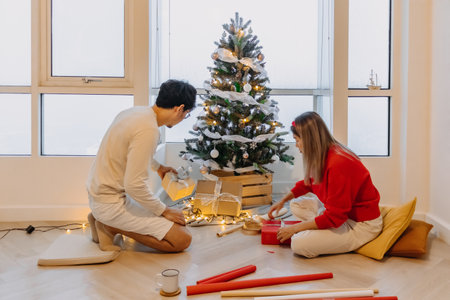 Asian husband and wife couple lover decorating Christmas tree together while the man helping woman packing decoration boxes.の写真素材