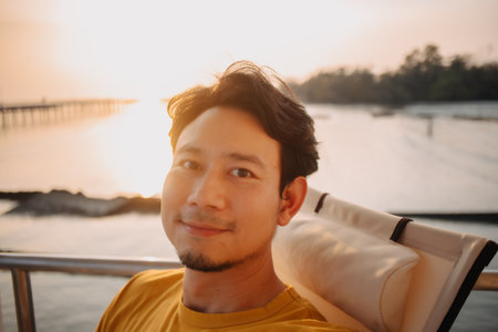 Portrait of happy smile Asian man selfie himself sits and relax for holiday trip in the resort with sunset sea view.の写真素材