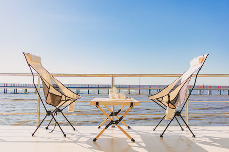 Set of picnic camping with folding chair and table, Manual grinder and coffee press, beautiful bright sky and ocean vacation.の写真素材