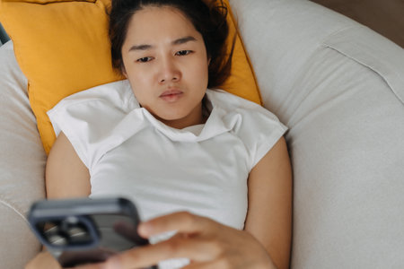 Sad and depressed Asian woman using mobile phone looking at the social media and get mental illness.